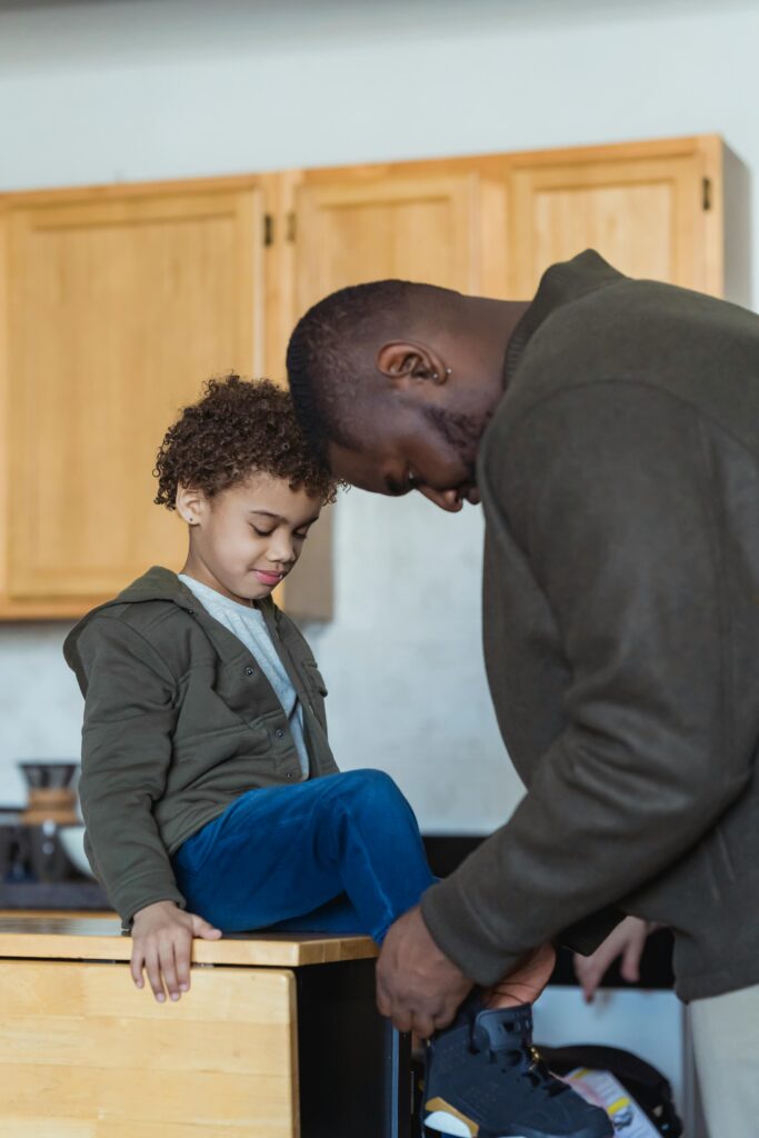 A father assists his young son in tying shoes, fostering a warm parent-child bond indoors.